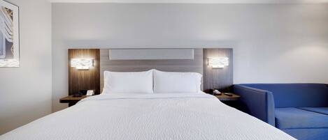 Habitación de hotel con una cama grande, dos mesitas de noche, un sillón azul y una lámpara de pared.