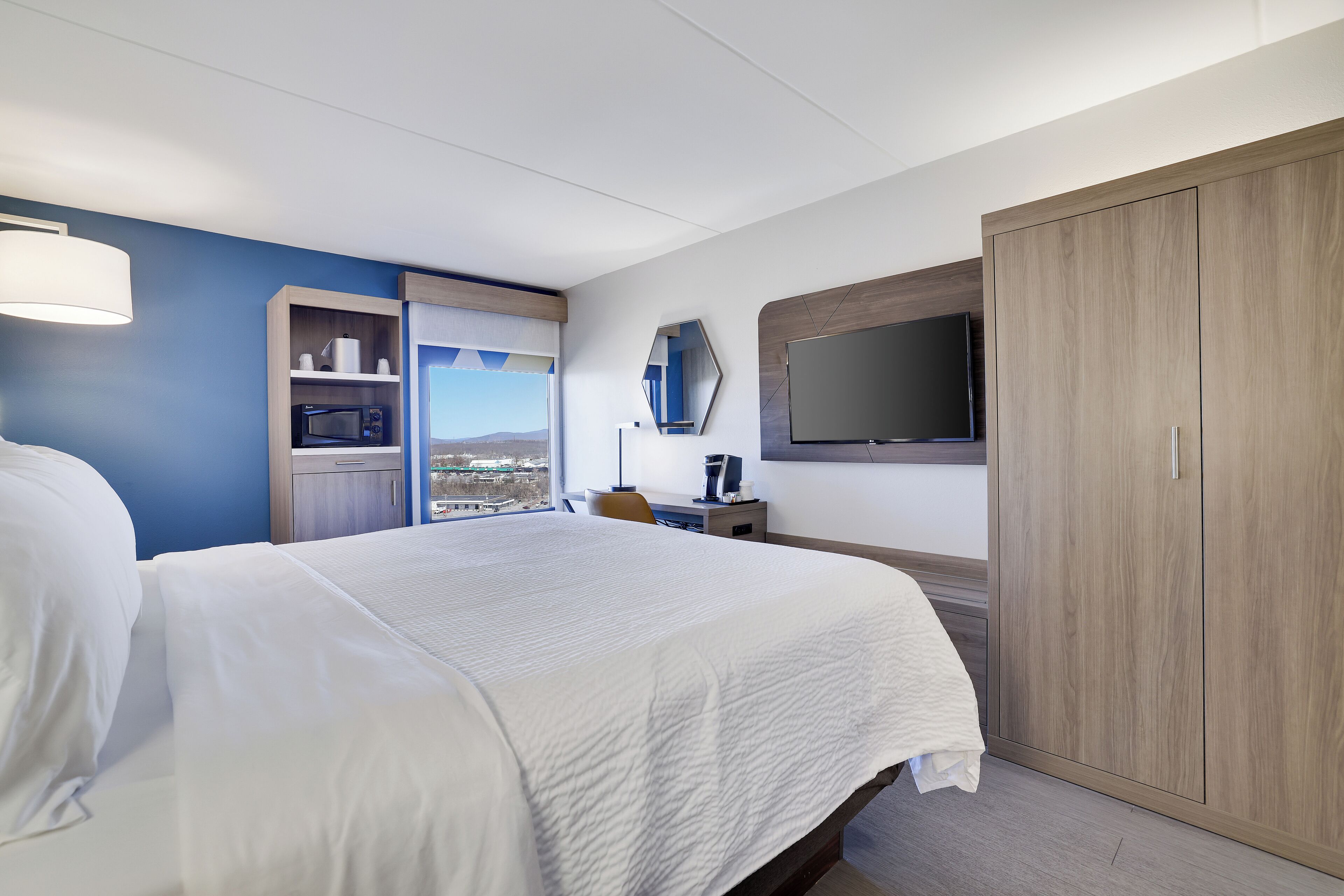 A hotel room with a large bed, a desk with a computer, a TV, and a wardrobe.