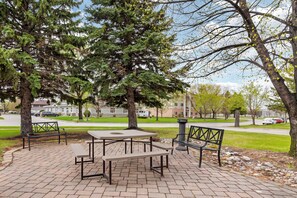 A park with picnic tables and benches, surrounded by trees and a building in the background.