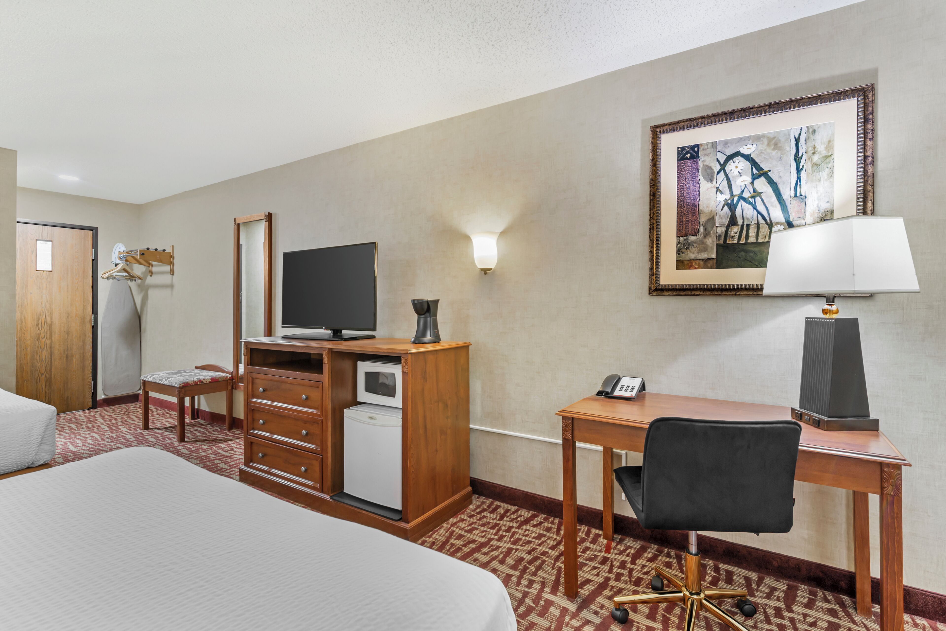 Una habitación de hotel con cama, escritorio, silla, televisión y un cuadro en la pared.