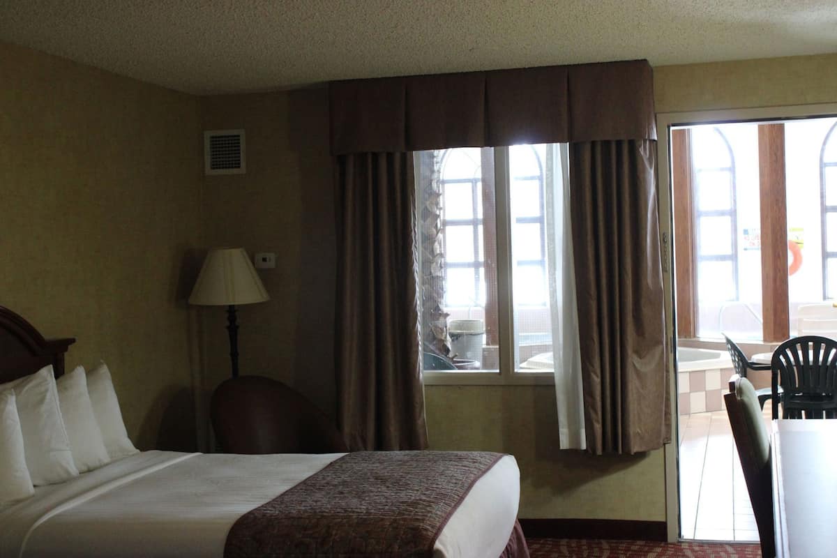 A hotel room with a bed, a chair, a lamp, a window with curtains, and a view of the outside.
