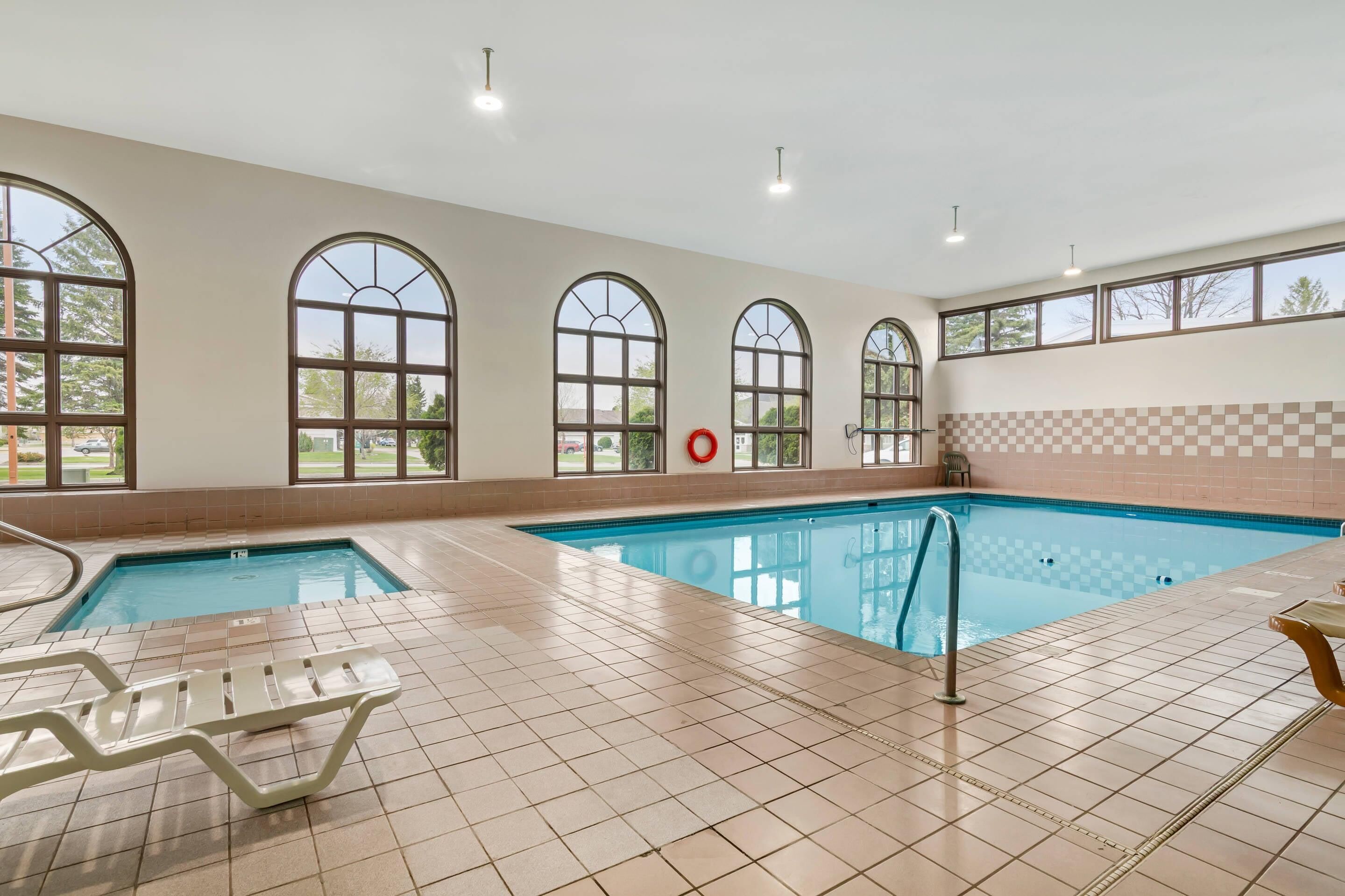 An indoor swimming pool with tiled floors, arched windows, and a red lifebuoy.