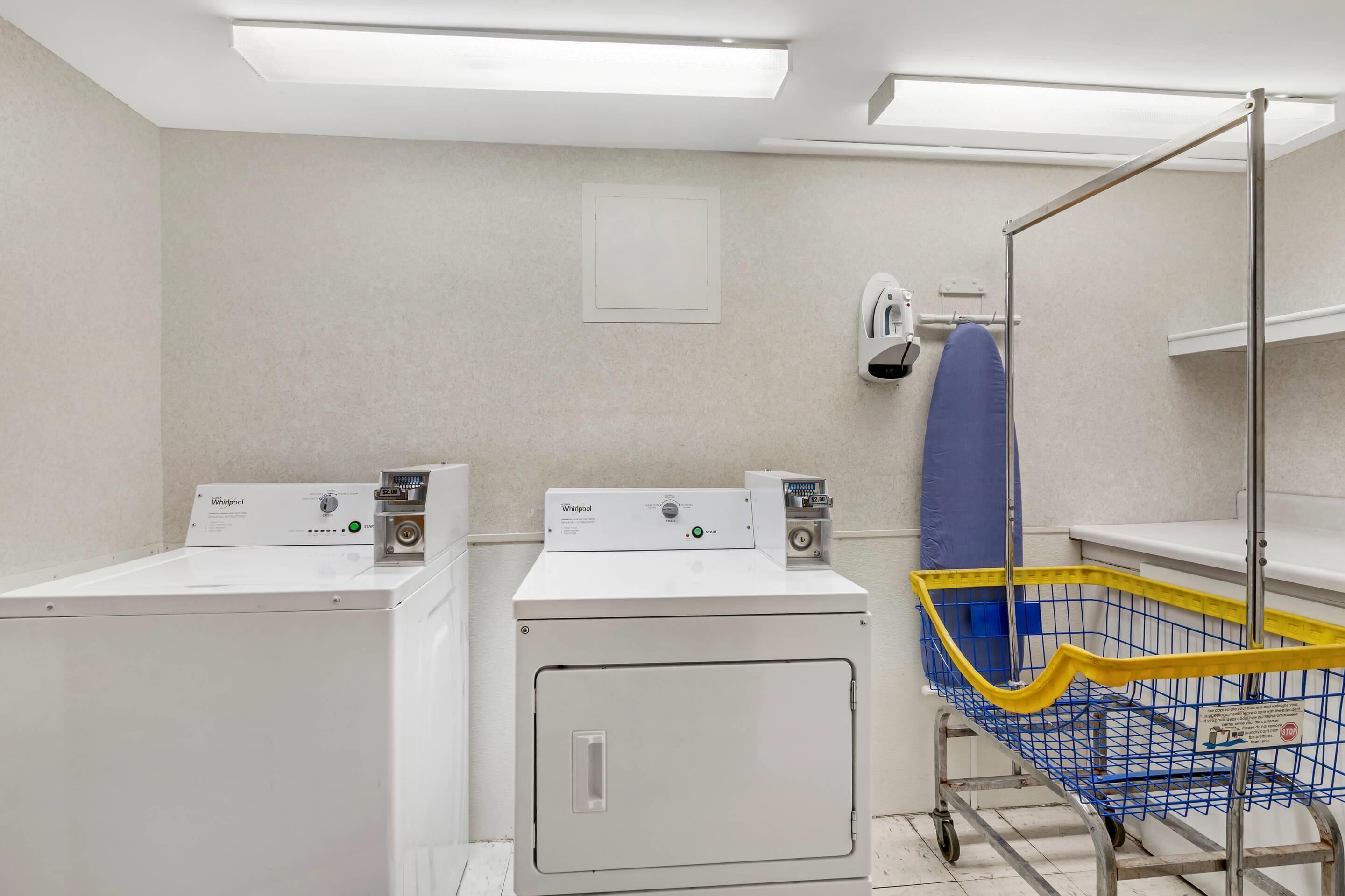 A laundry room with two Whirlpool washers, a blue and yellow cart, and a ceiling-mounted hand dryer.