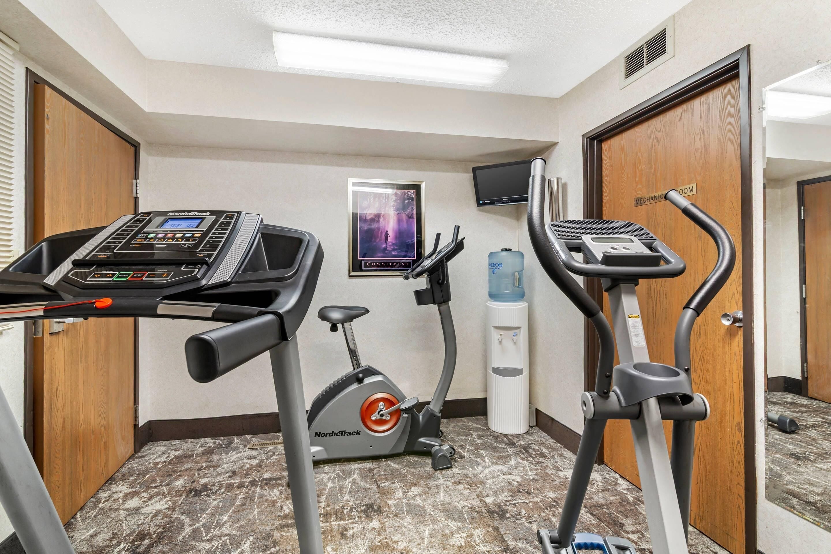 Un gimnasio con cintas de correr, elíptica y dispensador de agua.