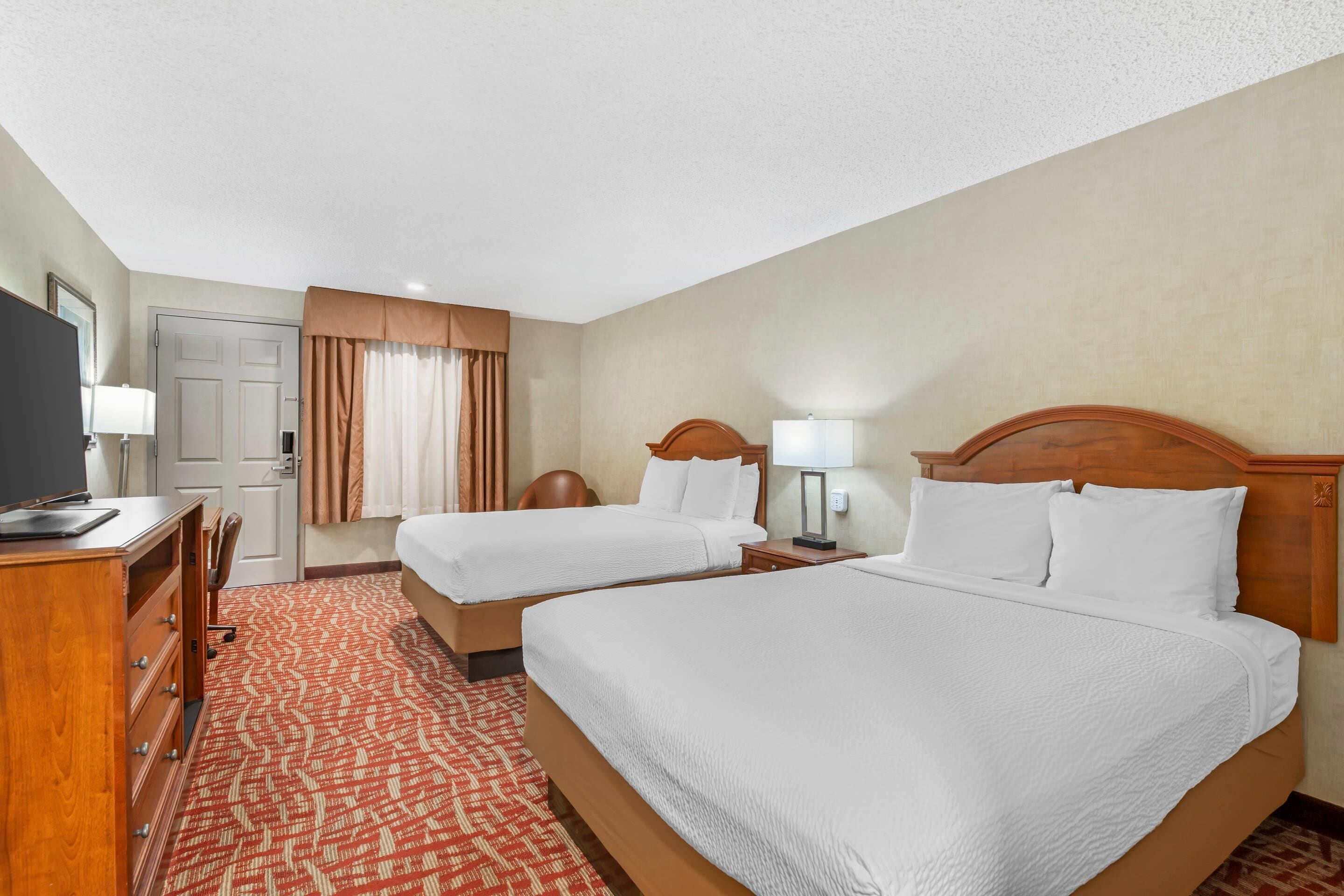 Une chambre d’hôtel avec deux lits, un bureau, une télévision et une porte.