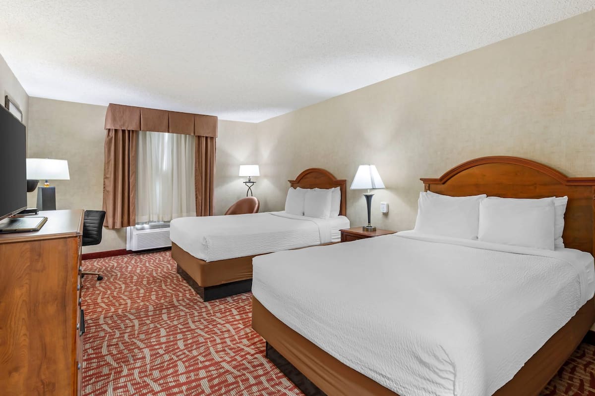 A hotel room with two beds, a desk, a chair, a lamp, and a window with curtains.