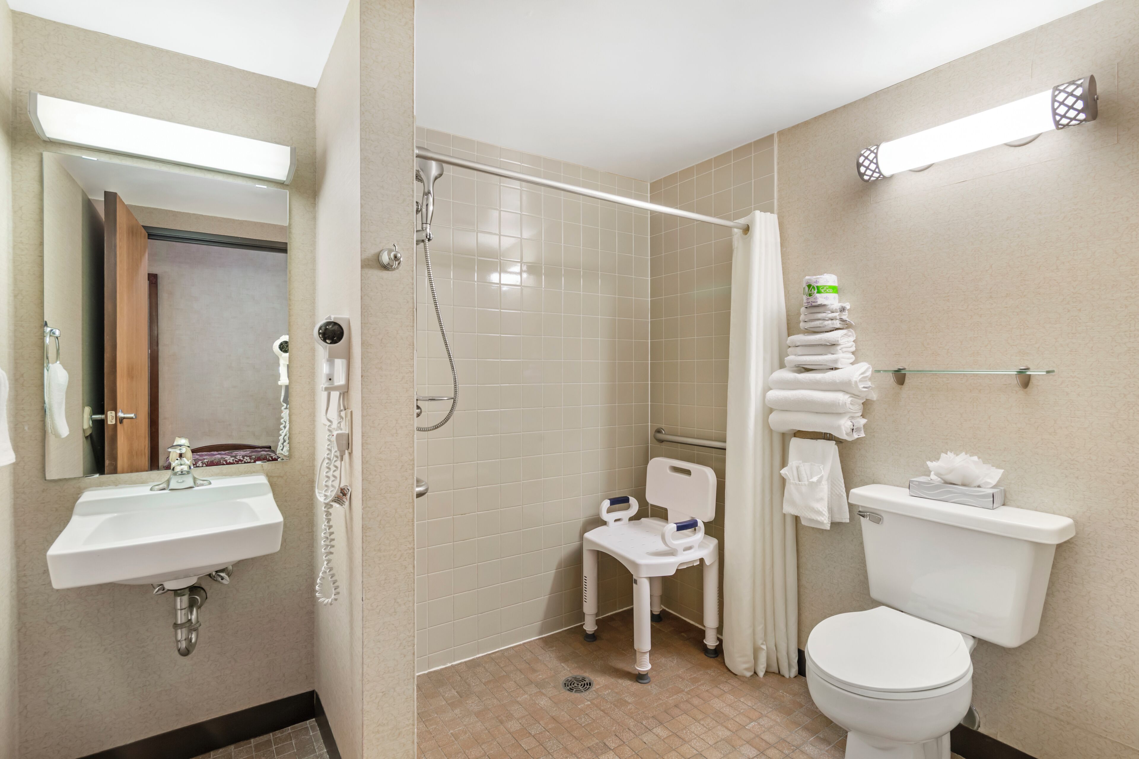 A bathroom with a sink, toilet, shower, and a wheelchair-accessible chair.