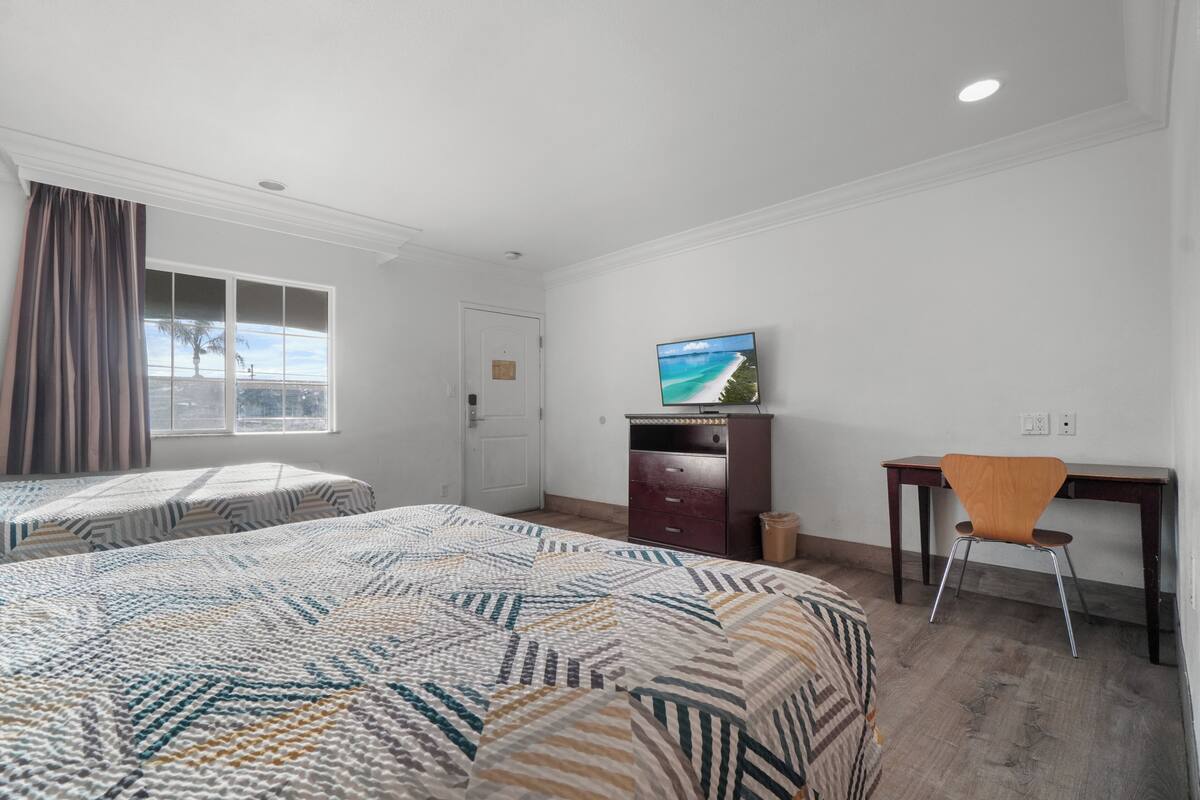 A hotel room with two beds, a desk, a TV, and a window with a view.