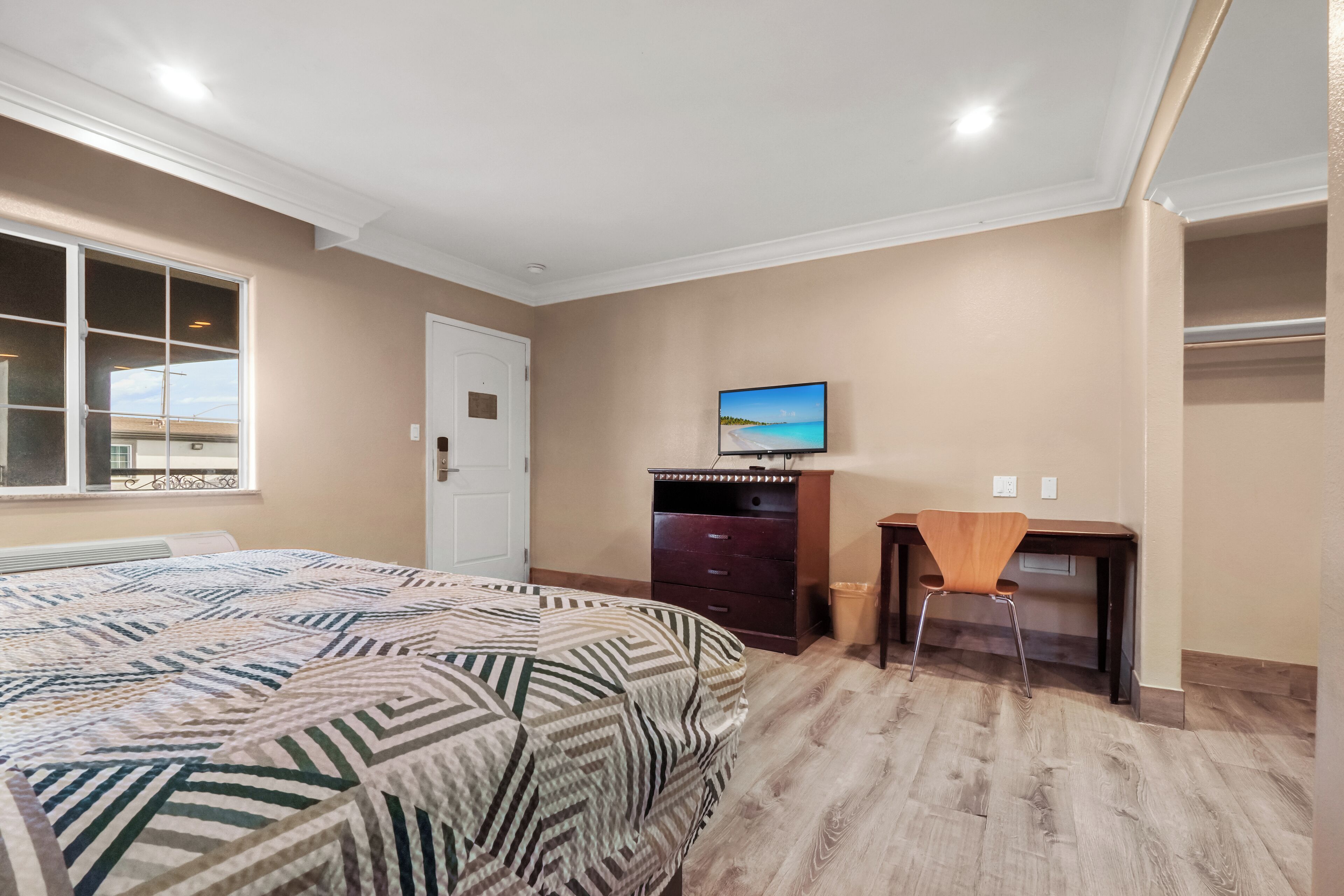 Une chambre à coucher avec un lit, un bureau, une chaise, une commode et un téléviseur fixé au mur.