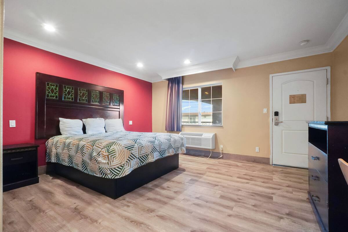 A bedroom with a bed, a nightstand, a wardrobe, a window, and a door.