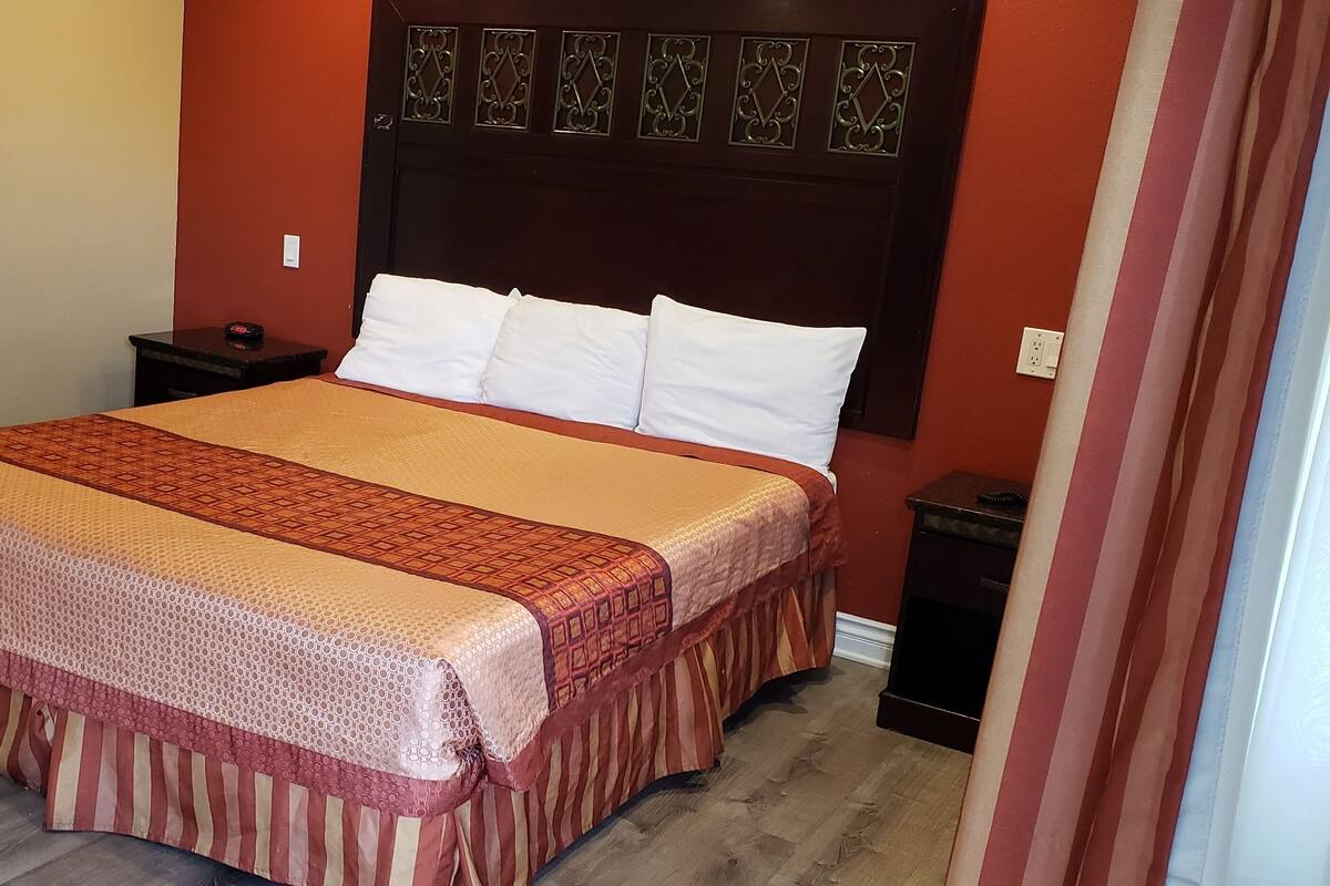 A neatly made bed with a patterned bedspread and pillows, a wooden nightstand with a lamp, and a dark headboard with decorative elements.