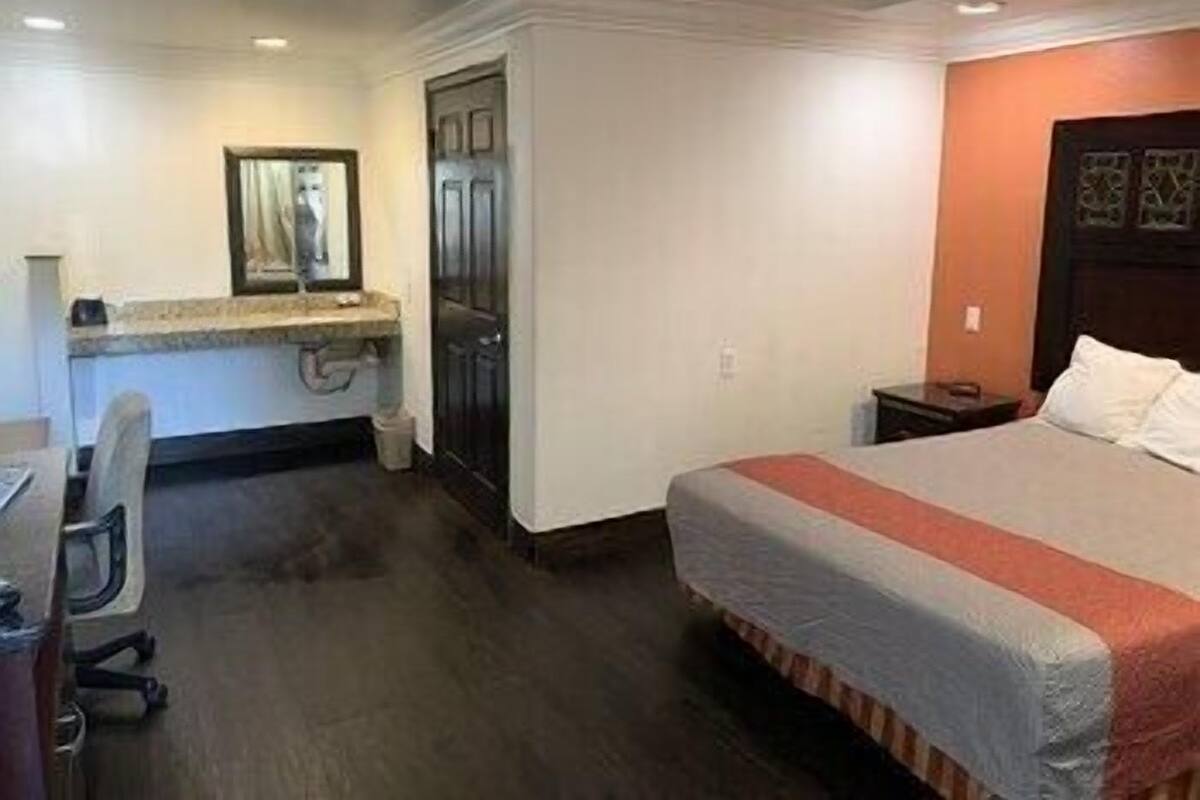 A hotel room with a bed, a desk, a chair, and a door.
