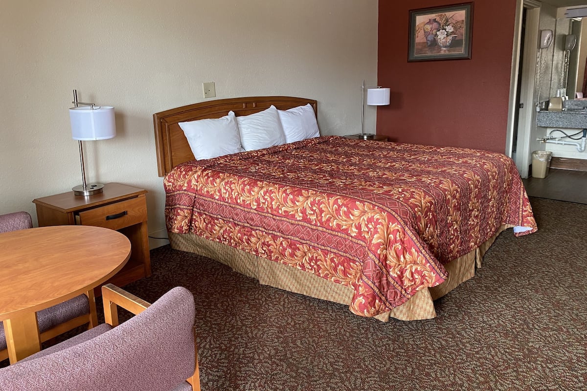 A hotel room with a large bed, a wooden nightstand, a desk with a chair, and a bathroom visible through an open door.