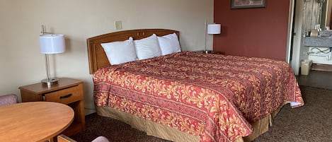 Habitación de hotel con una cama grande, una mesita de noche de madera, un escritorio con una silla y un baño a la vista a través de una puerta abierta.