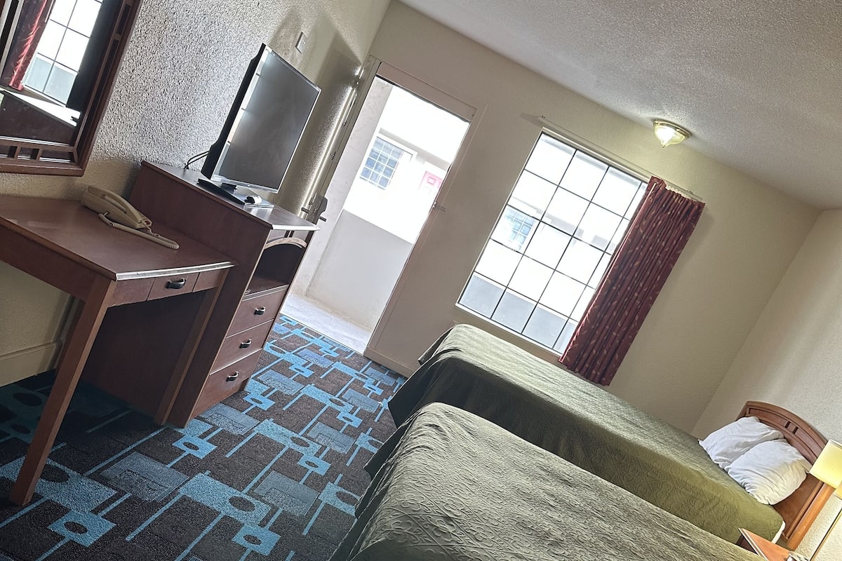 A hotel room with a bed, a desk with a telephone, a television, and a window with curtains.