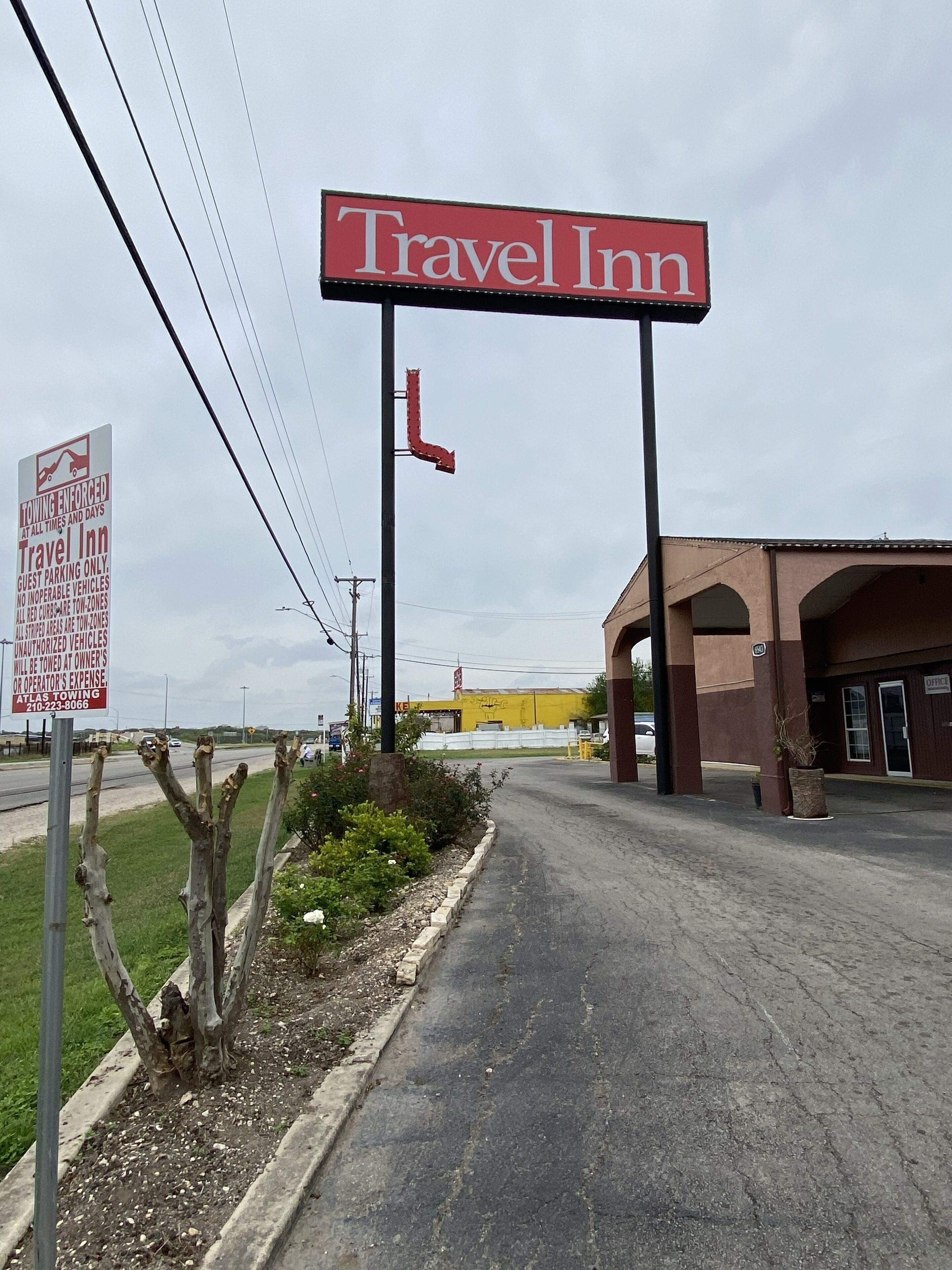 A Travel Inn sign, a parking sign, and a building with a yellow facade.