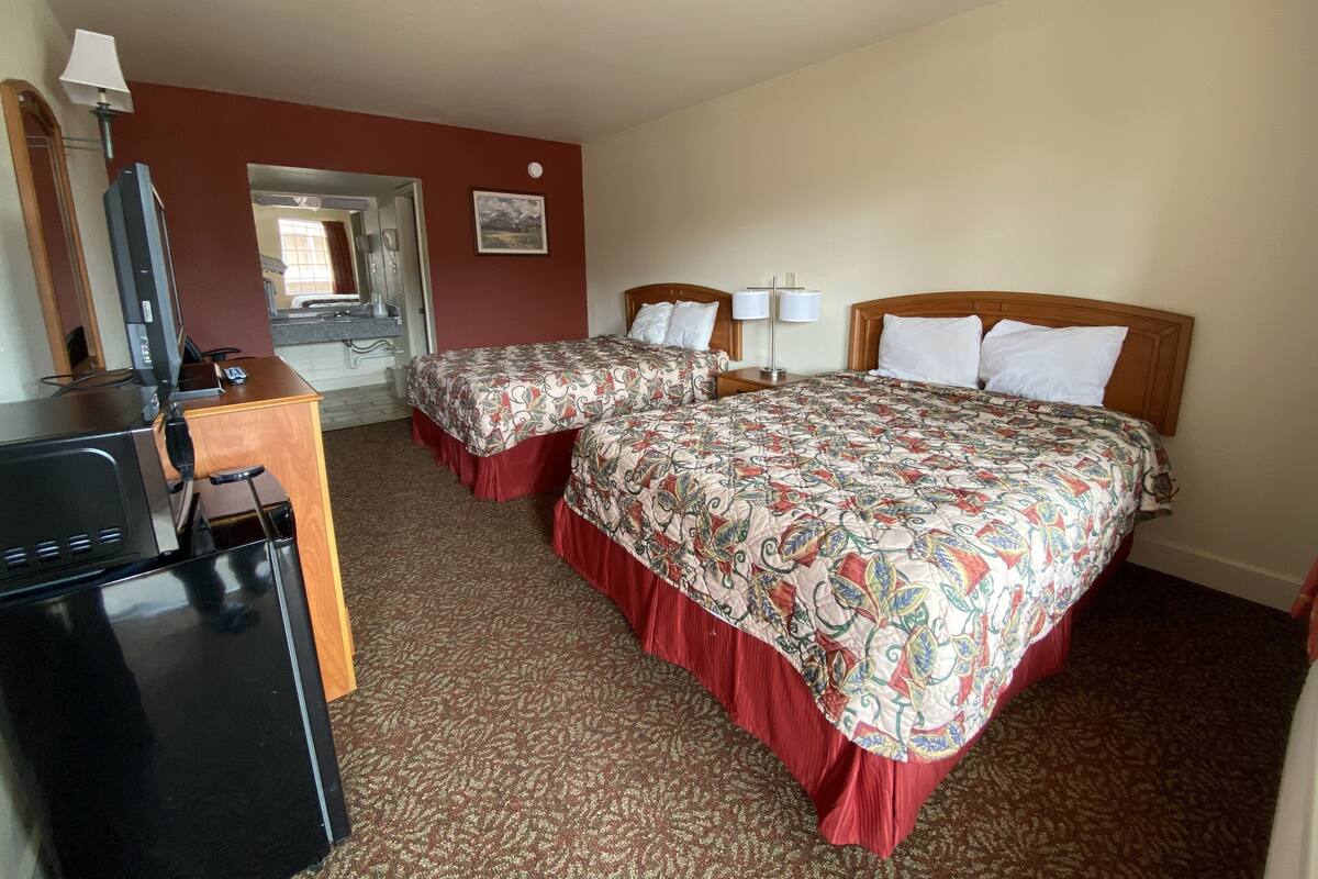 A hotel room with two beds, a desk with a computer, a mirror, and a door leading to a bathroom.