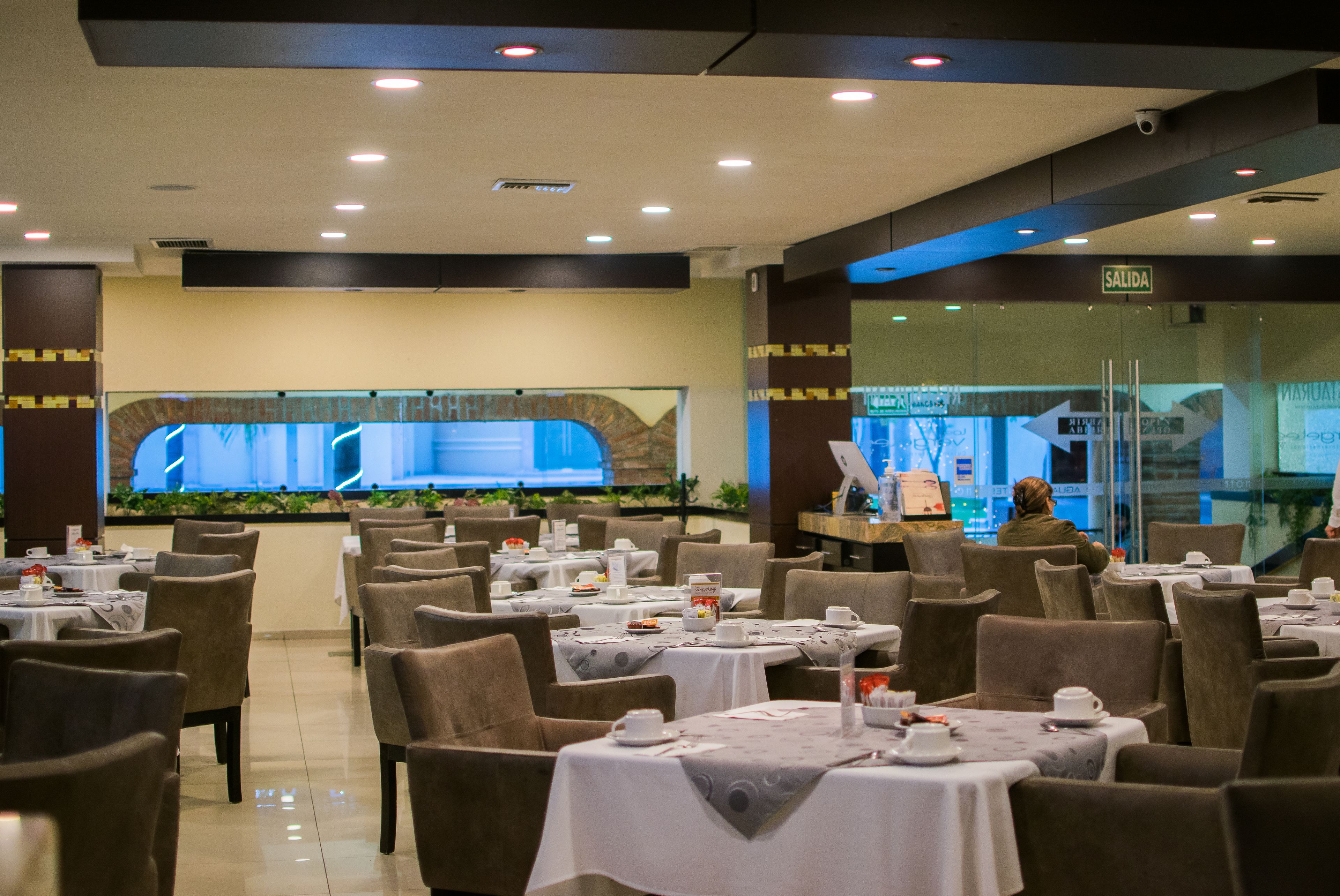 Een restaurant met gedekte tafels, een groot scherm waarop een presentatie draait, en een bord met de aanduiding van de uitgang.