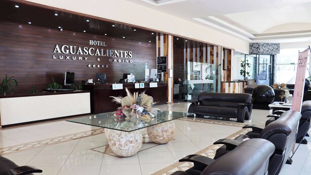 A hotel reception area with a modern design, featuring a reception desk, seating area, and a glass coffee table with decorative items.