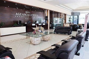 A hotel reception area with a modern design, featuring a reception desk, seating area, and a glass coffee table with decorative items.
