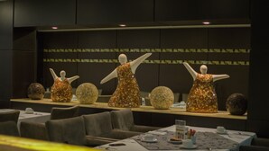 A dining area with tables set for service, a reception desk, and decorative spherical objects on the wall.