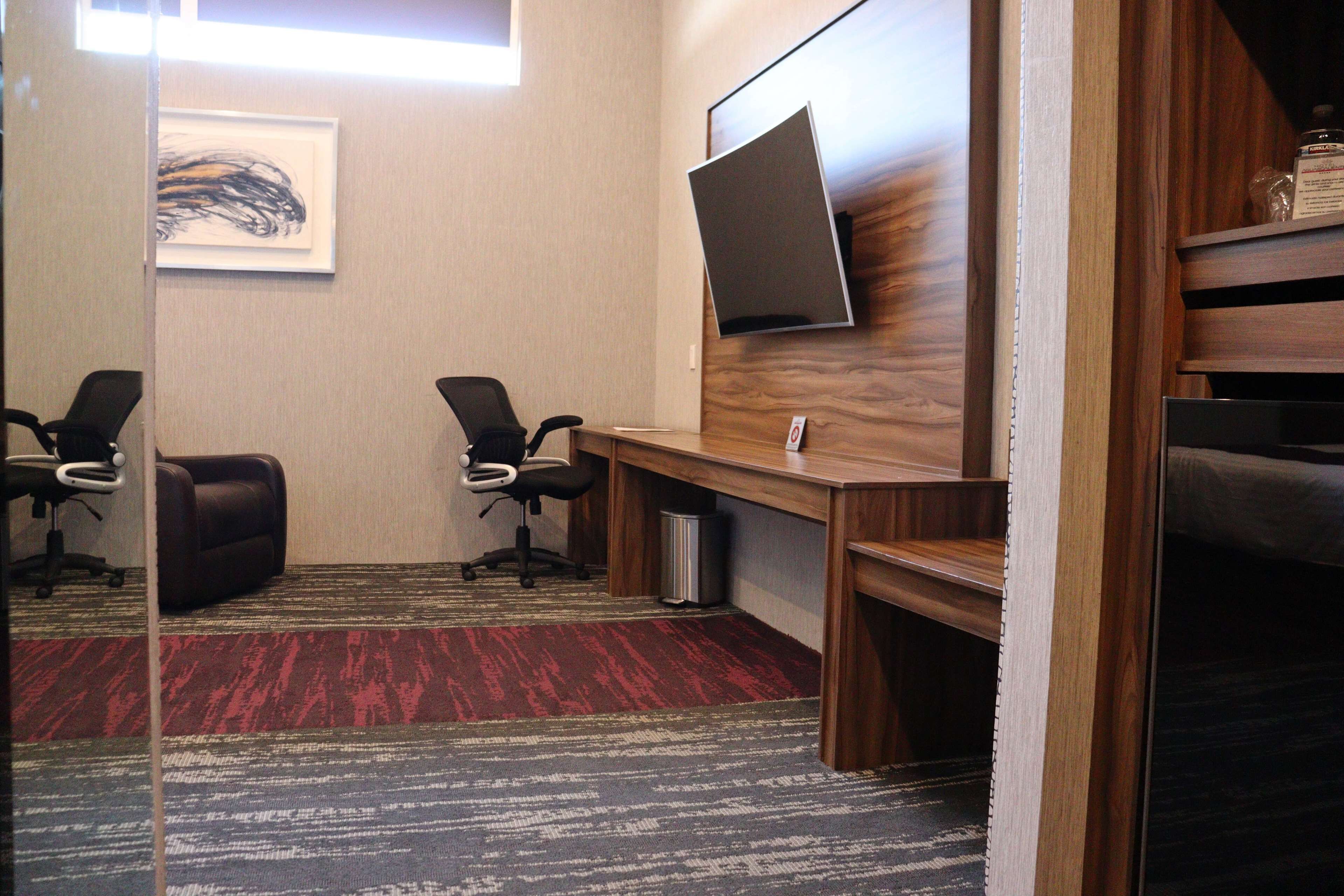 A conference room with two black office chairs, a wooden desk, a mounted flat-screen TV, and a red and gray carpet.