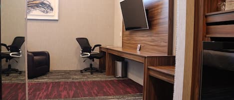 A conference room with two black office chairs, a wooden desk, a mounted flat-screen TV, and a red and gray carpet.