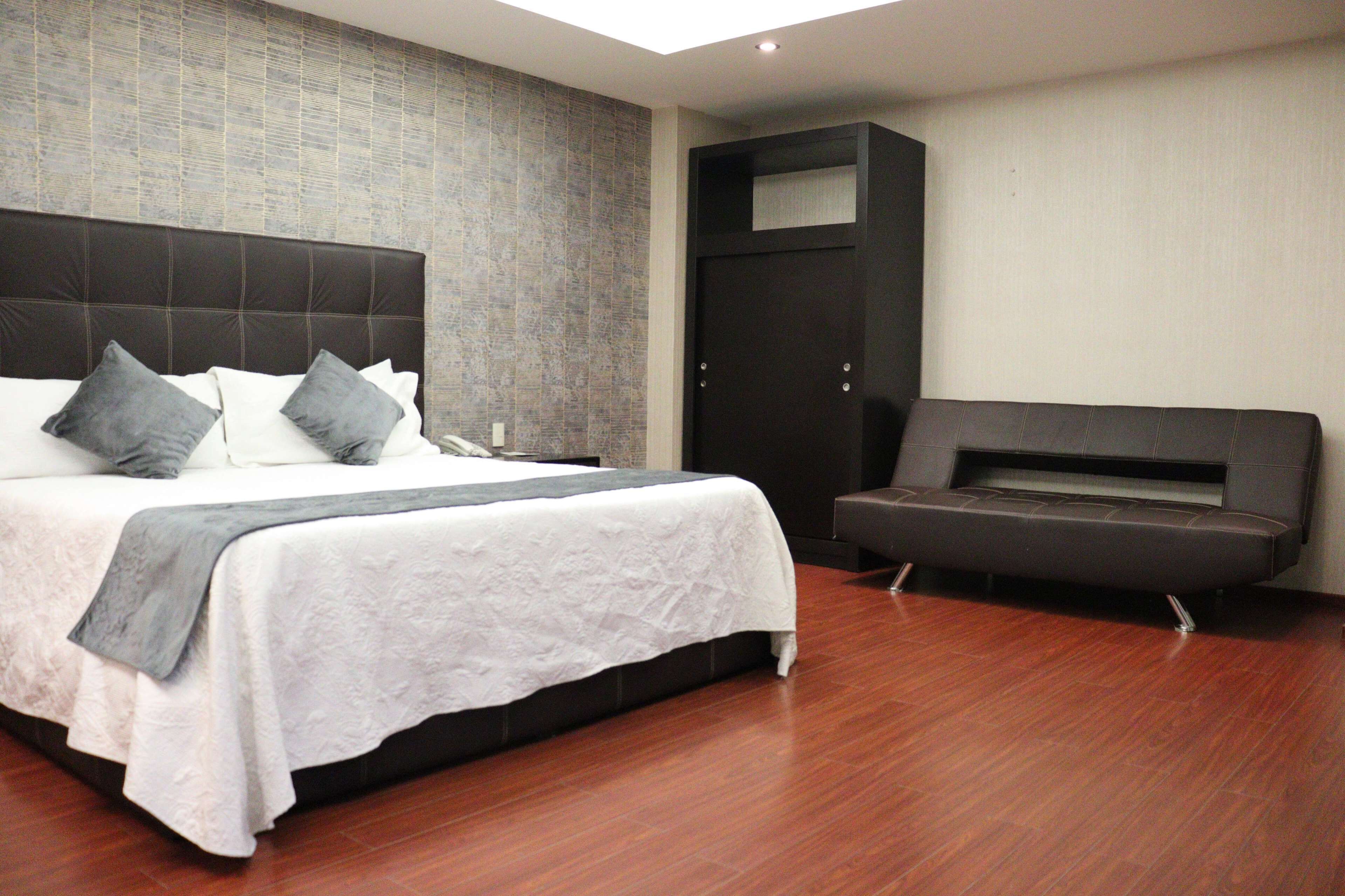A modern bedroom with a large bed, a dark wardrobe, and a built-in bench.
