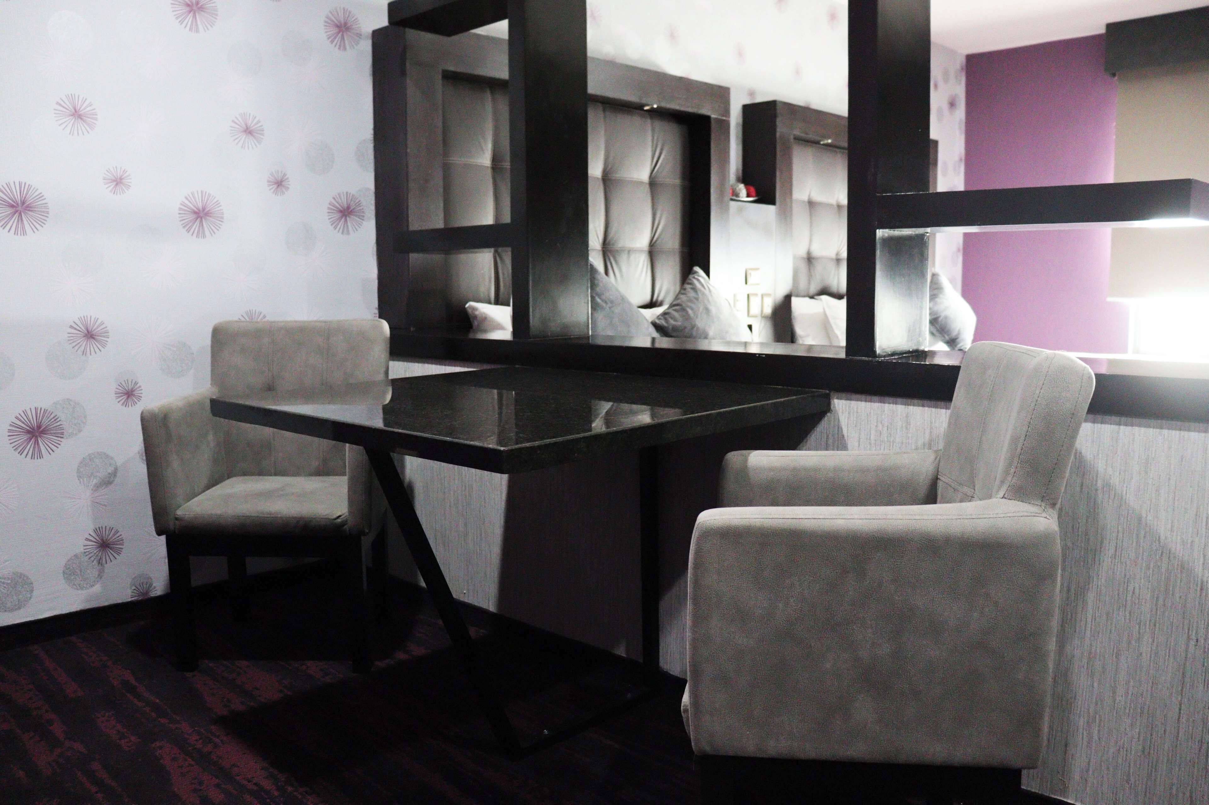 Una habitación con un espejo grande, dos sillas, una mesa de madera oscura y un papel tapiz estampado.