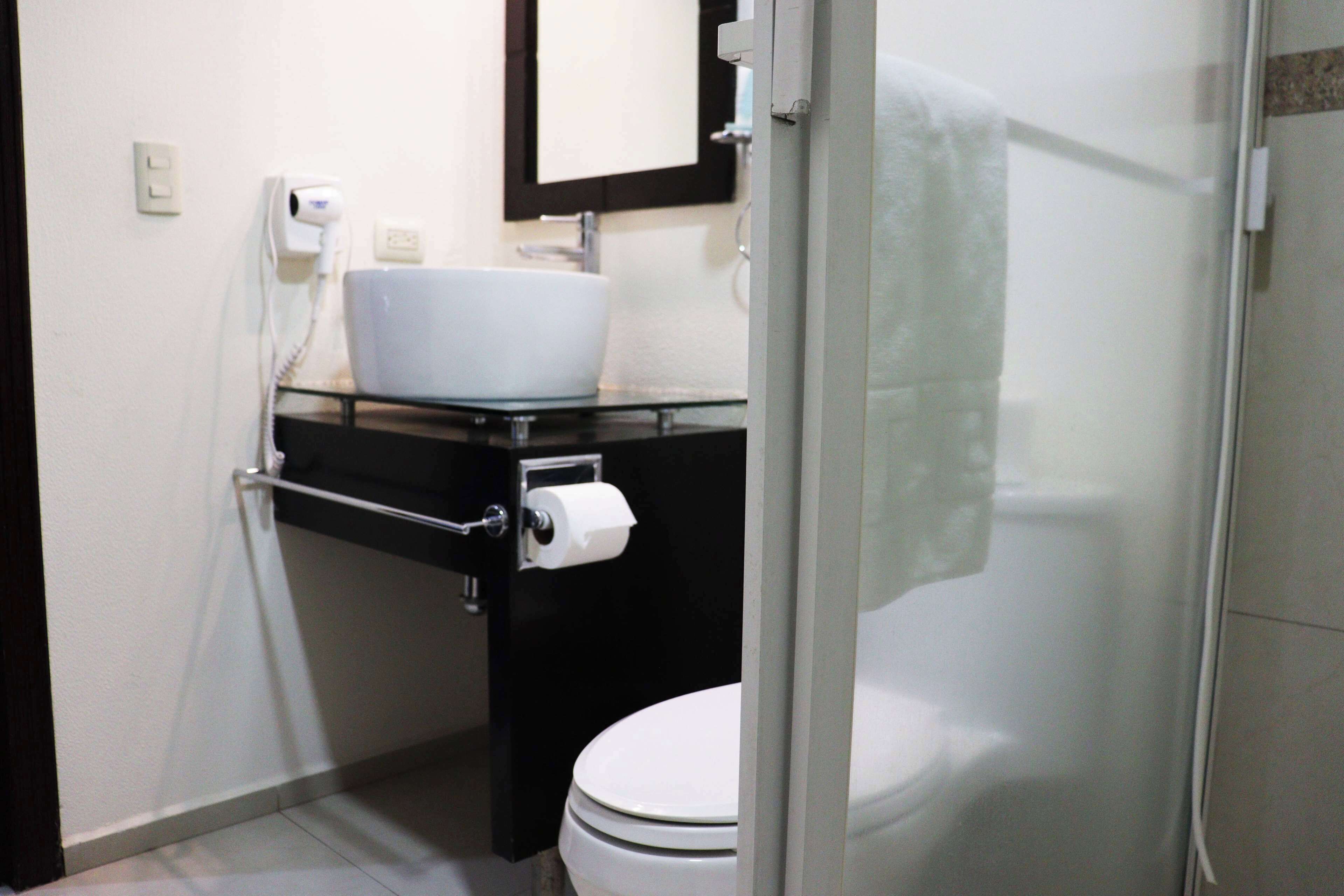 Un baño con inodoro blanco, lavabo de cristal y un espejo.