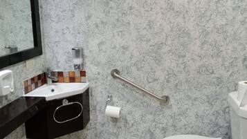Un baño con pared de diseño marmolizado, un lavamanos negro con espejo, un inodoro y un pasamanos.