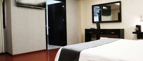 A hotel room with a bed, a flat-screen TV, a mirror, a dresser, and a door leading to another room.