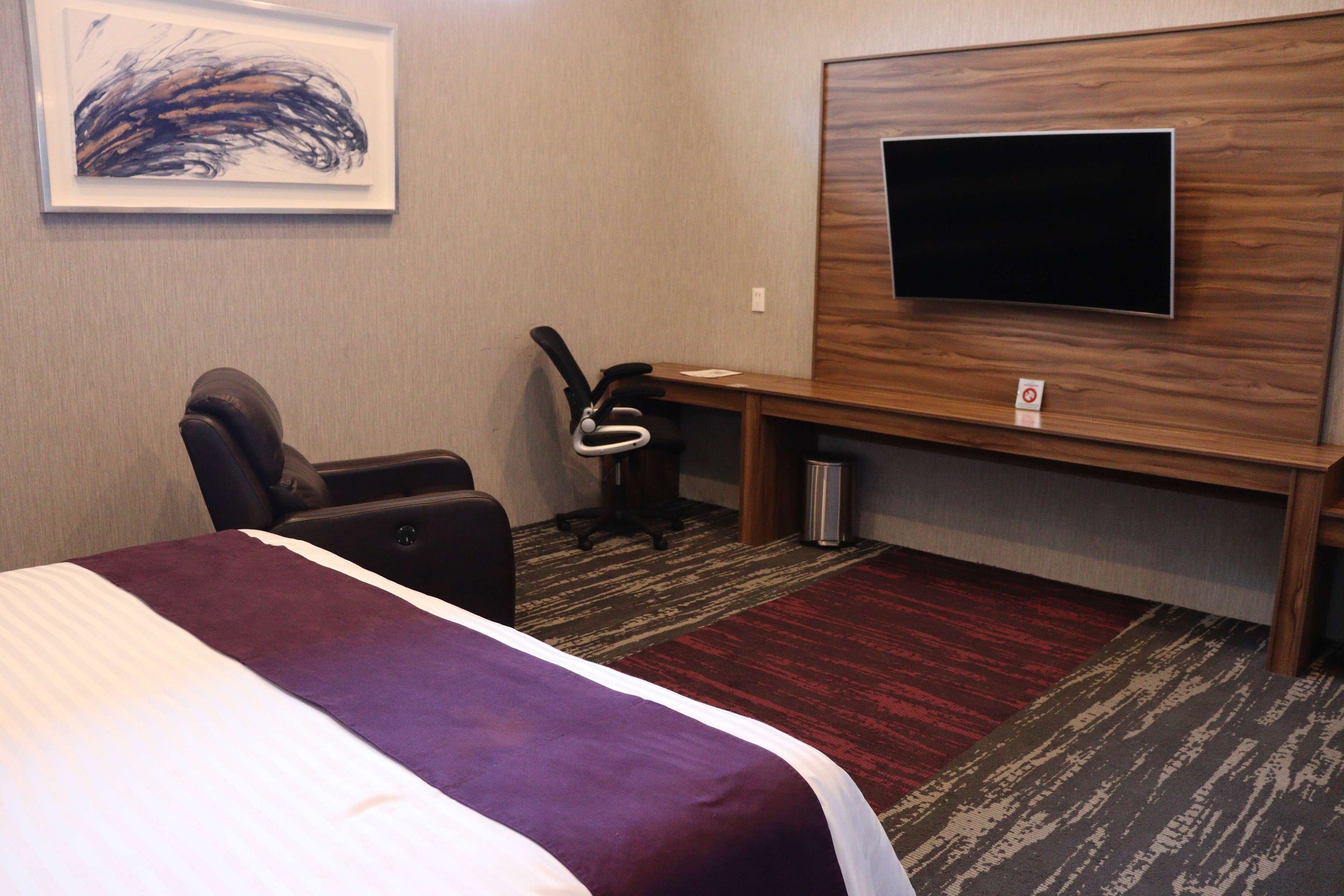 A hotel room with a bed, a desk, a chair, a television, and a carpeted floor.