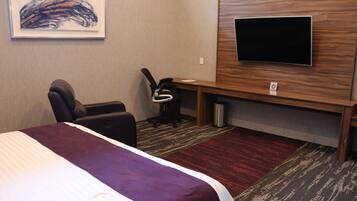 A hotel room with a bed, a desk, a chair, a television, and a carpeted floor.