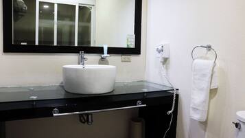 Un baño con lavamanos blanco, encimera negra y espejo arriba.