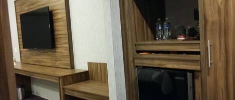 Een kamer met een houten tv-meubel, een bankje en een klein kastje met flessen.