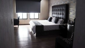 A modern hotel room with a large bed, a bedside table, a chair, and a window with a view.