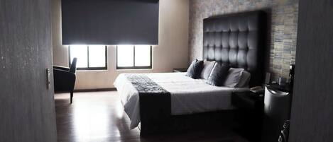 Una habitación de hotel moderna con una cama grande, una mesita de noche, una silla y una ventana con vistas.
