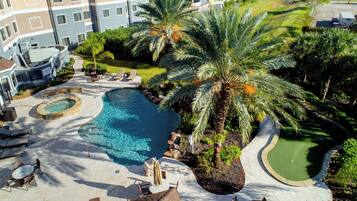 A swimming pool surrounded by palm trees and lounge chairs, with a building in the background.