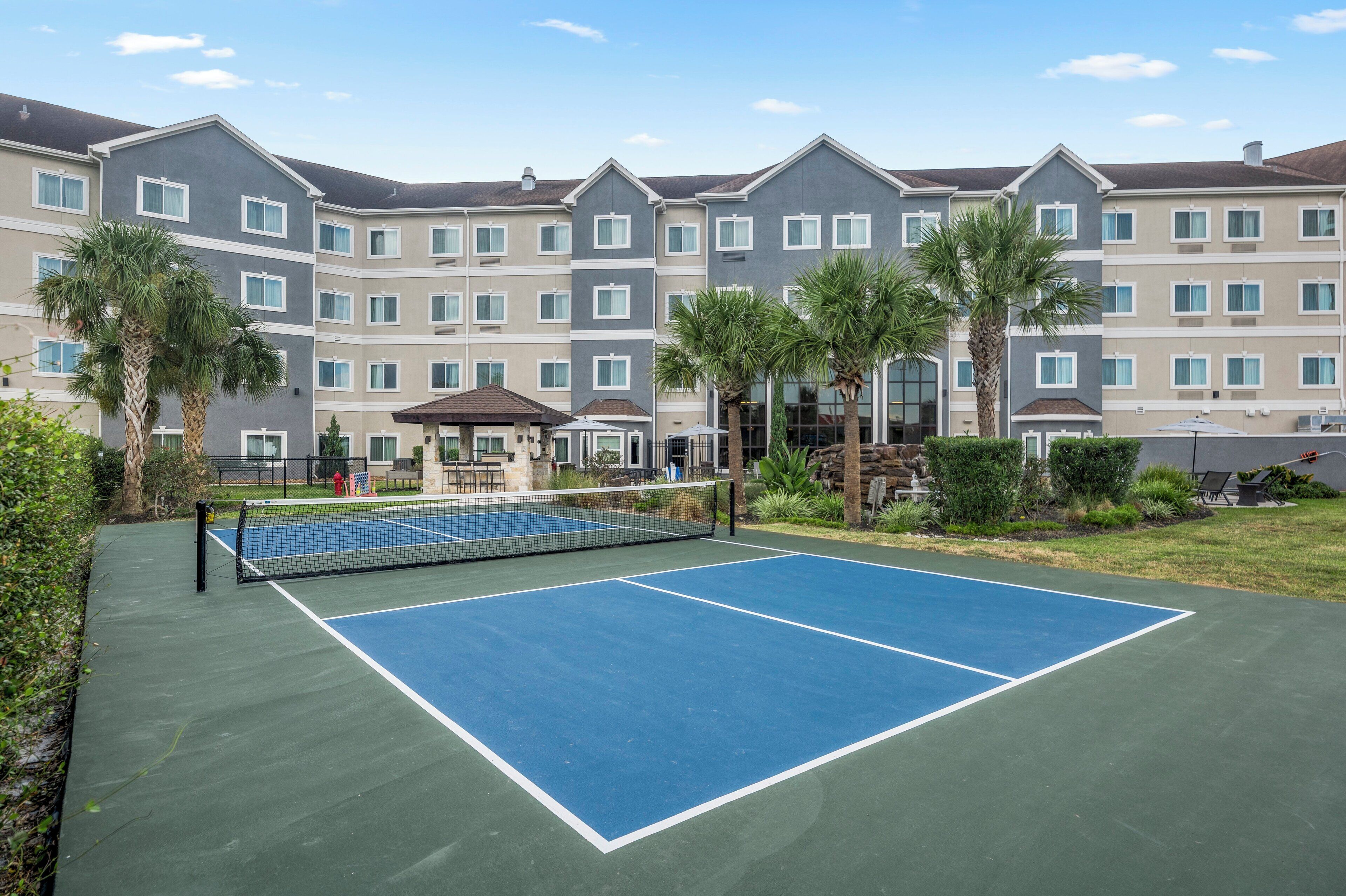 A tennis court with a net, surrounded by a building with multiple floors and balconies.
