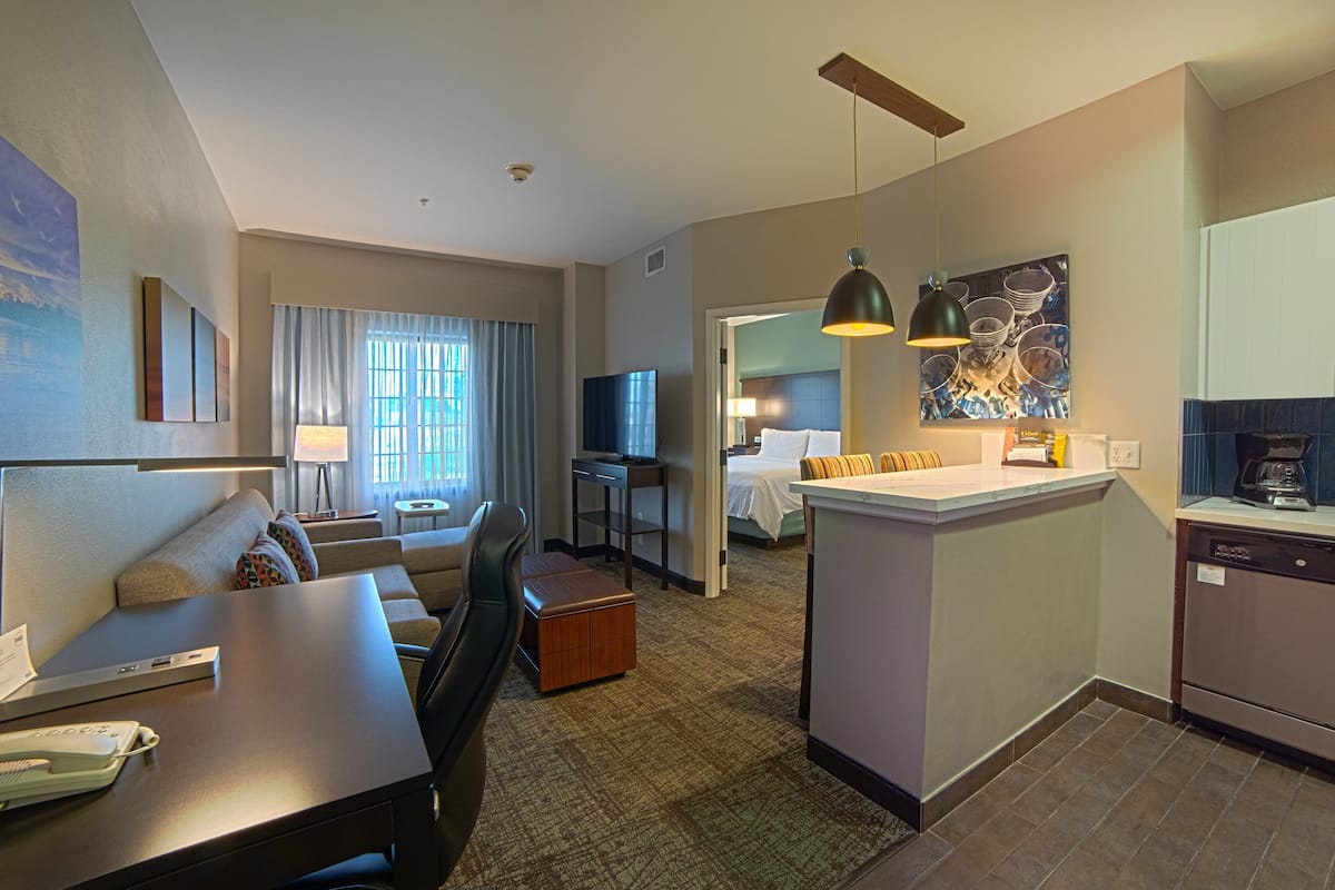 Habitación de hotel con sofá, escritorio, zona de comedor, cocina y baño.