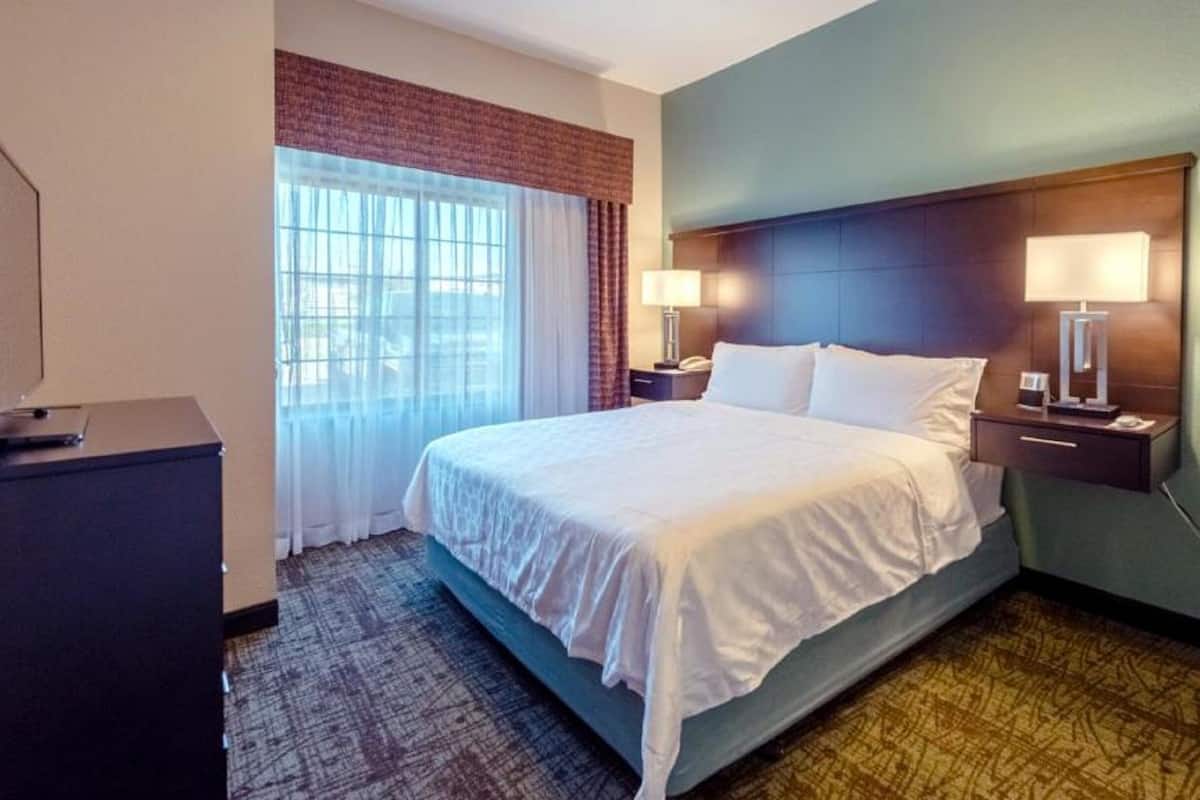 Habitación de hotel con una cama grande, dos mesitas de noche con lámparas, un escritorio con computadora y una ventana con cortinas.