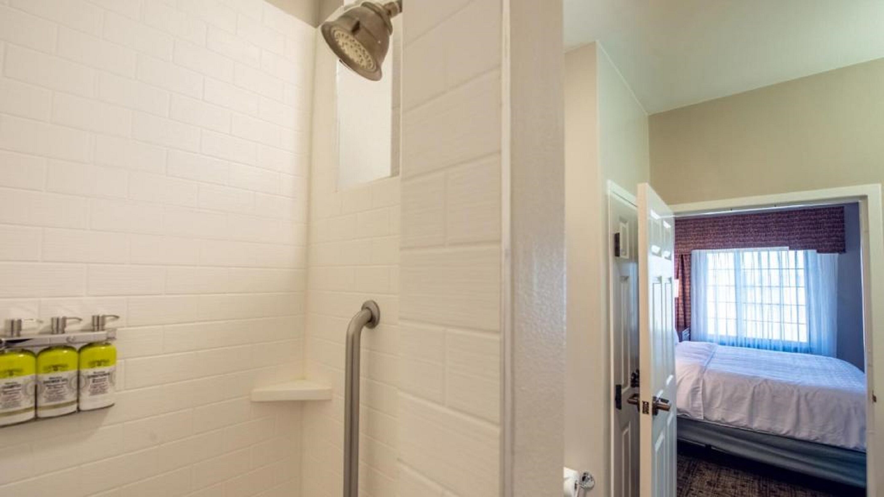 A hotel room with a shower, a bed, and a window with curtains.