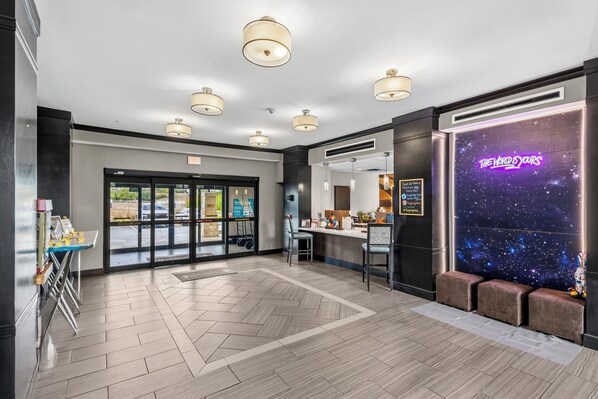 A hotel lobby with a reception desk, seating area, and a neon sign.