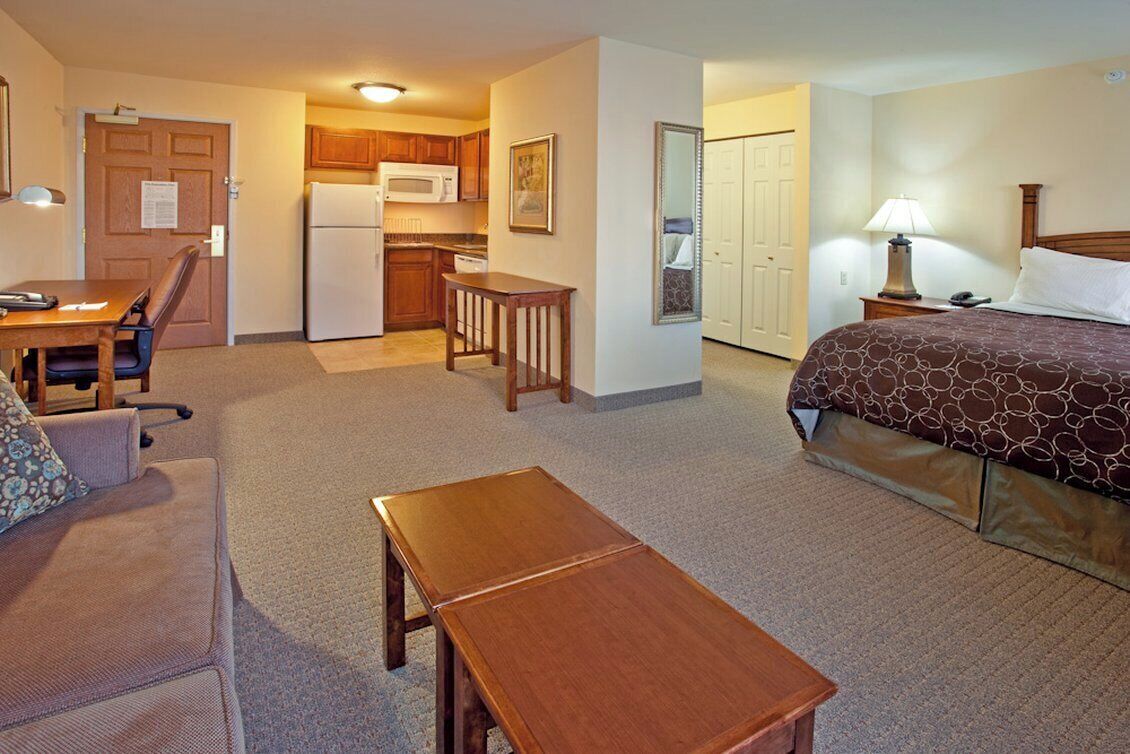 Ein Hotelzimmer mit Bett, Schreibtisch, Stuhl, kleinem Tisch, einer Küchenzeile und einem Badezimmer.