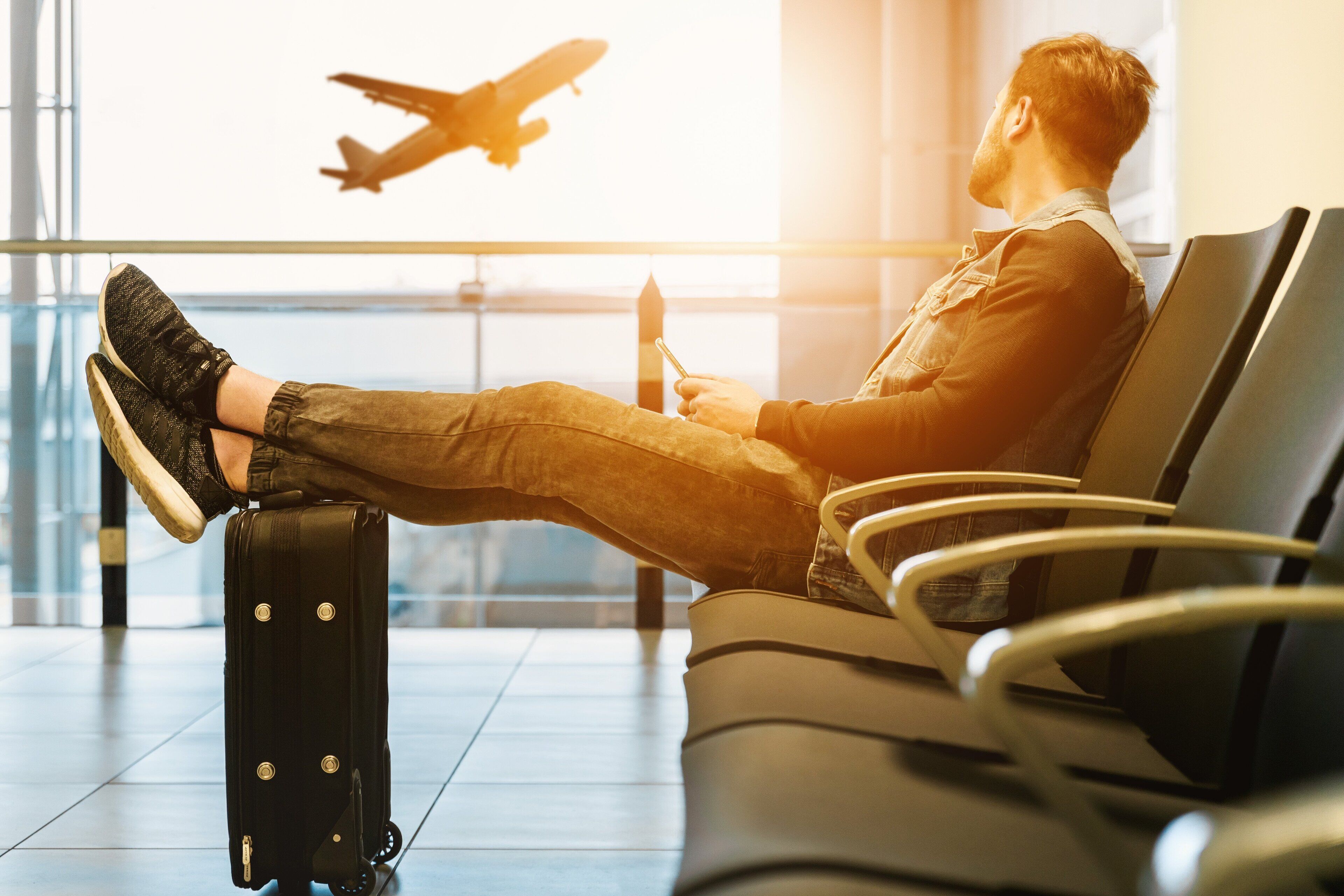 A person sitting on a chair with a suitcase beside them, an airplane flying in the background.