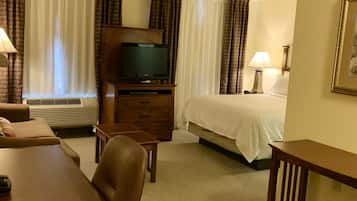 Une chambre d’hôtel avec un lit, un bureau, une chaise, un téléviseur posé sur un meuble en bois et une fenêtre avec des rideaux.