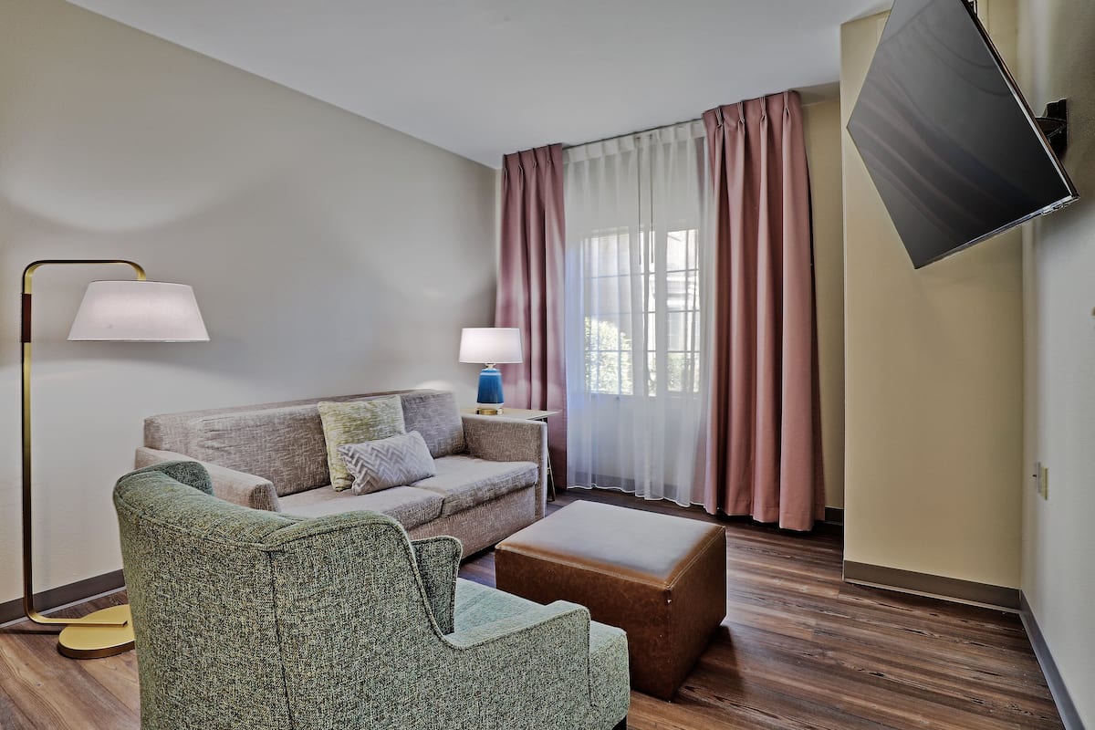 Un salon moderne comprenant un canapé, un fauteuil, un pouf, une lampe sur pied et un téléviseur à écran plat fixé au mur.