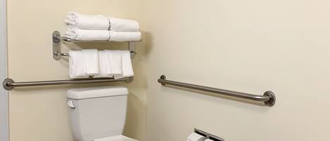A bathroom with a toilet, handrails, a towel rack, and a sink.