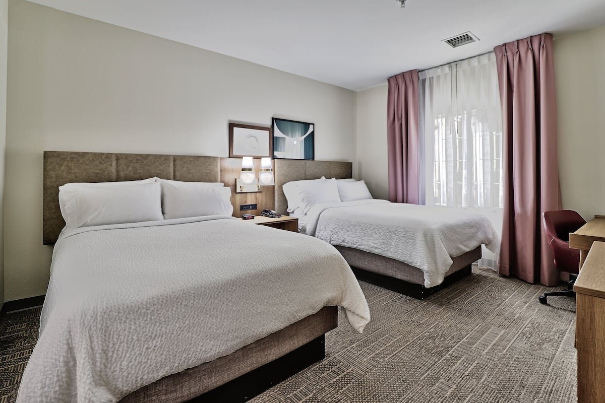 Une chambre d’hôtel avec deux lits, un bureau, une chaise et une fenêtre avec des rideaux.
